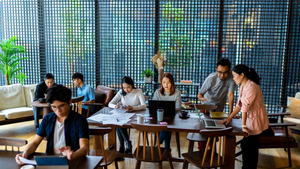 Egy modern irodai környezet, ahol fiatalok dolgoznak laptopokon és beszélgetnek.