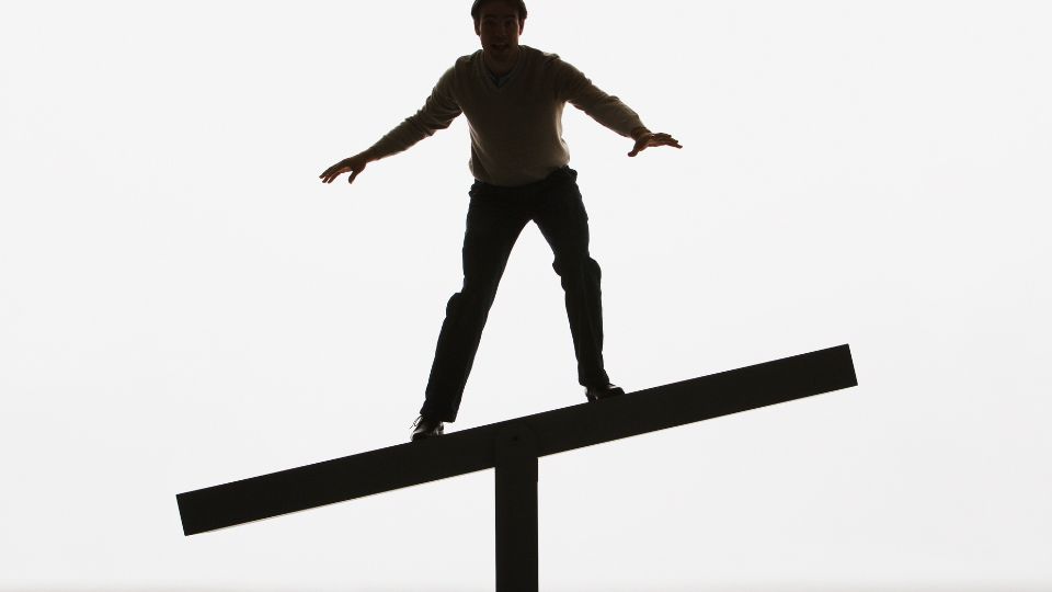 Egy férfi egyensúlyozik egy vízszintes rúdon, háttérben világos fényekkel.