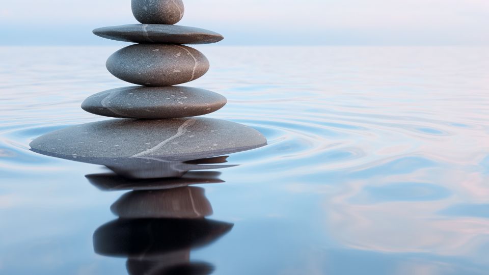 Egy vízszintes vízfelszínen álló, gondosan elhelyezett kövek toronyja, amely a nyugalmat sugallja.