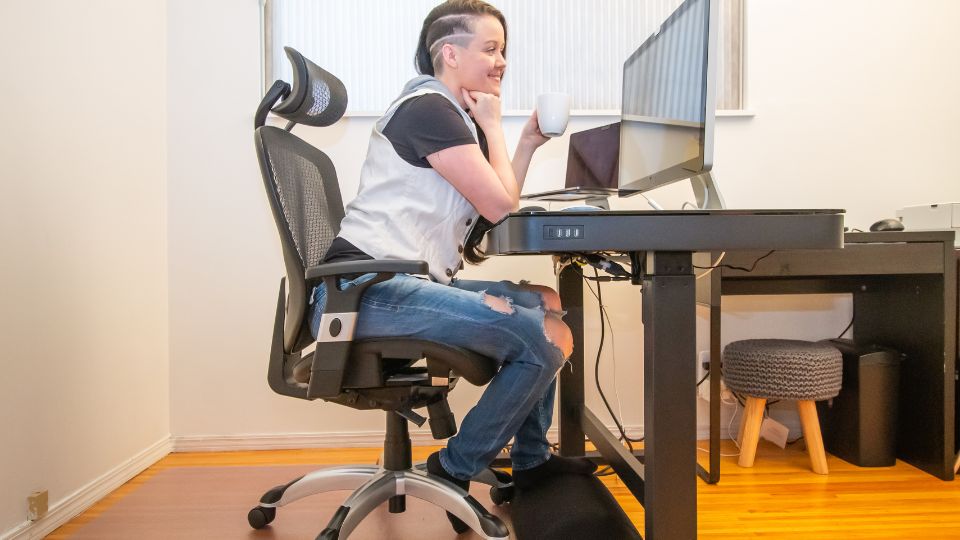 Egy fiatal nő ül egy modern íróasztalnál, miközben egy bögrét tart a kezében.