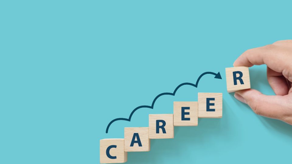 Egy kéz fa kockákat mozgat, amelyek a karrier szót alkotják, kék háttér előtt.