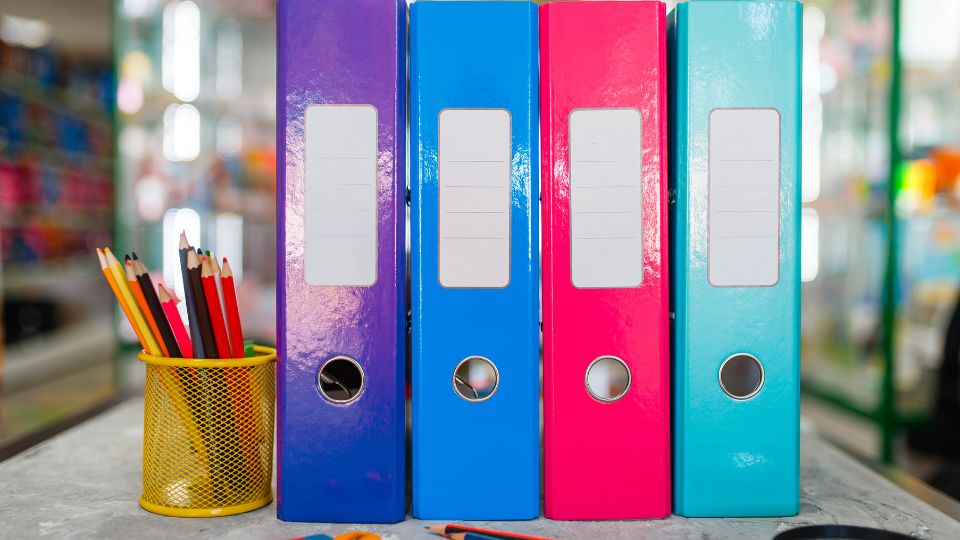 Színes irattartók és ceruzák egy íróasztalon, rendezett irodai környezetben.