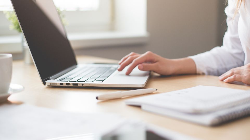 Egy üzleti laptop használata, kéz a billentyűzeten, íróeszközök az asztalon.